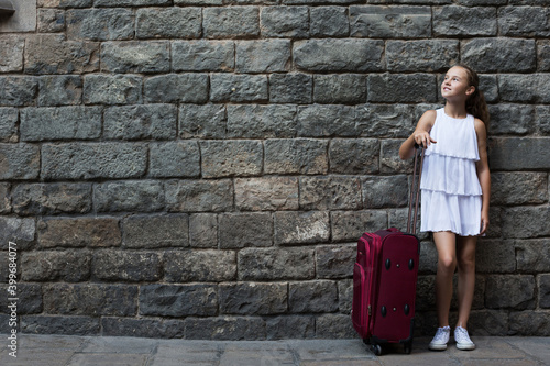 Happy girl in white with travelling bag on stone wall background