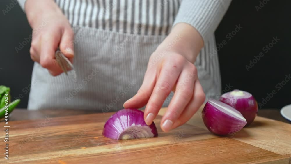 A close-up look of slicing the red onion on a wooden cutting board in ...