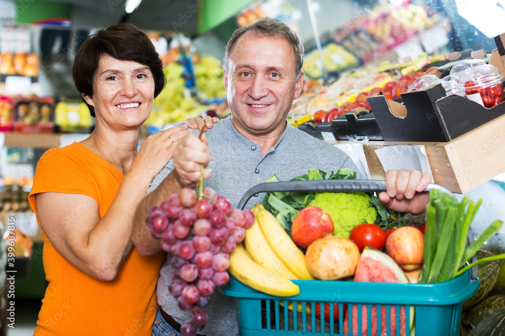 Mature man and his wife are demonstraiting basket with assortment goods in supermarket