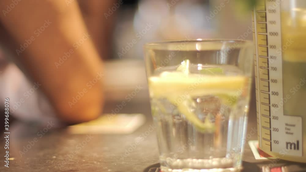 Close up of a a glass of lemonade with a lemon slice in it and a person sitting in the blurred background. Close up of a a glass of lemonade with a lemon slice in it and a person sitting in the blurred background.