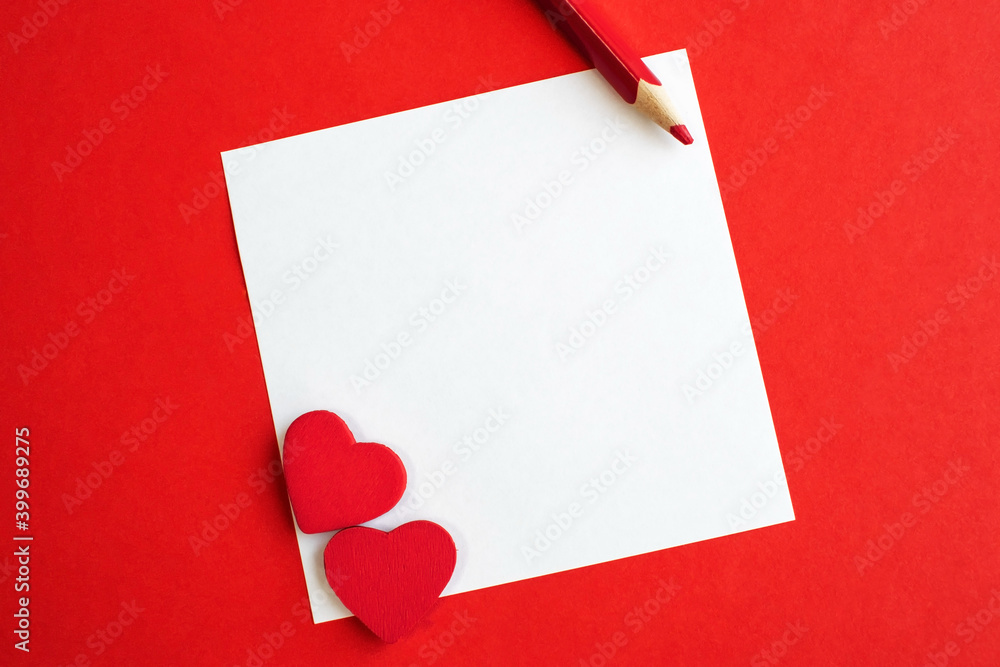 a white square sheet of paper with a red heart and pencil on a red background. Holiday background with space for text. a white square sheet of paper with a red heart and pencil on a red background. Holiday background with space for text.
