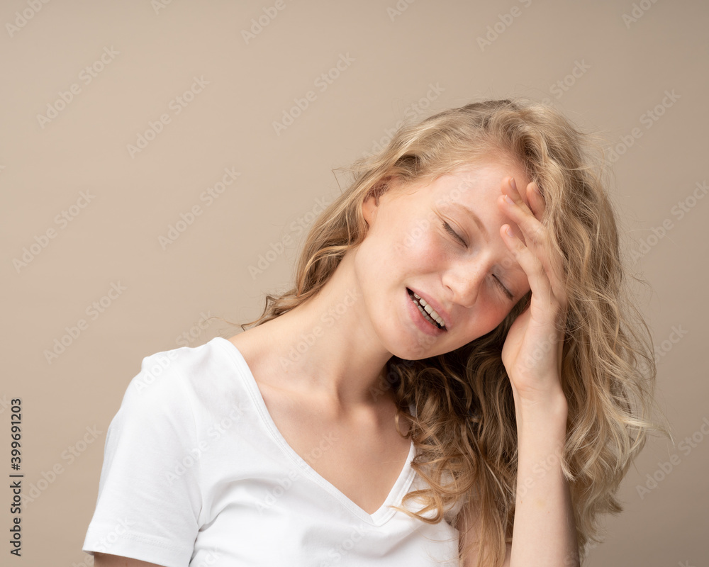 Unhappy woman putting hand on head due to headache after, filling with deep sadness. Migraine. on beige wall. Pretty female with curly hair in white t shirt Unhappy woman putting hand on head due to headache after, filling with deep sadness. Migraine. on beige wall. Pretty female with curly hair in white t shirt