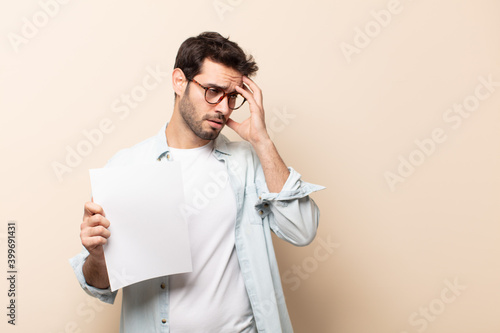 young handsome man feeling bored, frustrated and sleepy after a tiresome, dull and tedious task, holding face with hand photo