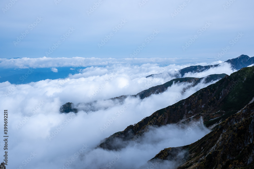 View of rocky mountain range and valley engulfed in clouds on the horizon in early autumn at Senjojiki Cirque in Nagano Prefecture, Japan.