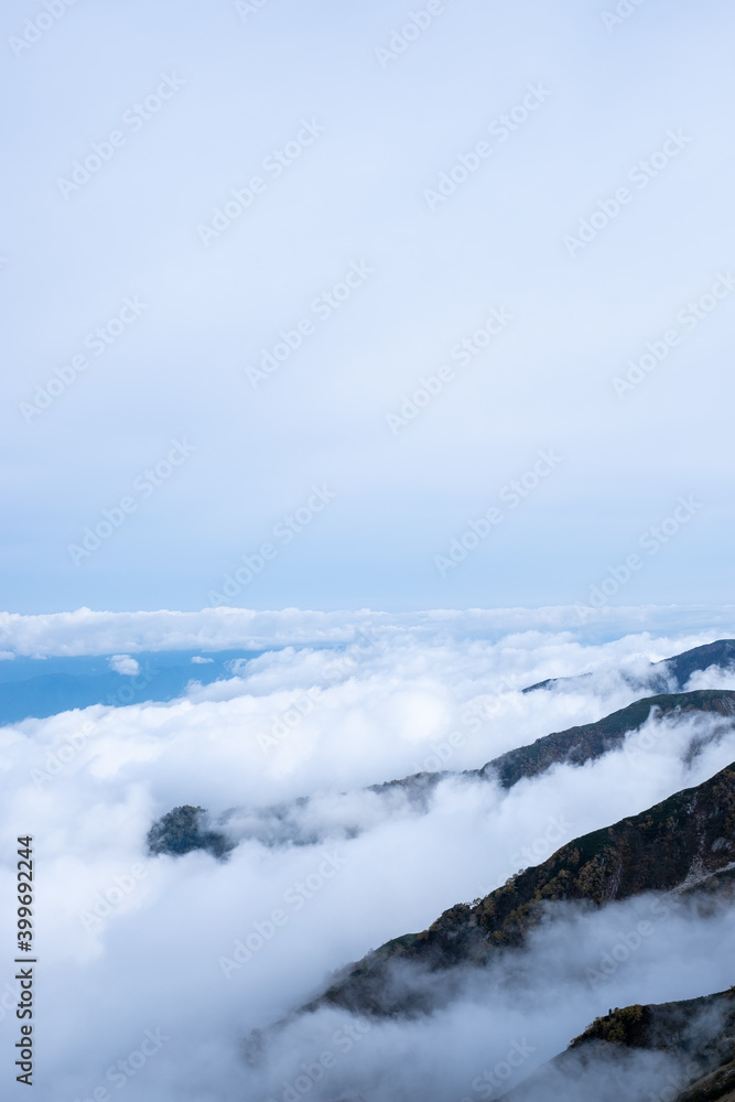 Obraz premium View of rocky mountain range and valley engulfed in clouds on the horizon in early autumn at Senjojiki Cirque in Nagano Prefecture, Japan.