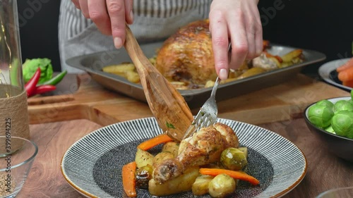 A chef is arranging roasted chicken and vegetables into a serving plate in 4k. Concept of serving food from an oven pan in slow-motion.