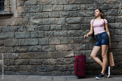 girl traveler with suitcase leaning against stone wall