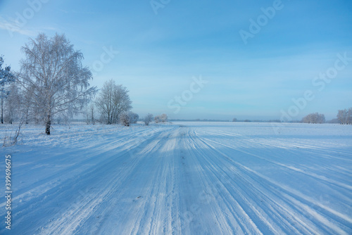 Snow covered winter field with trees and road going through to the horizon. Winter landscape. Beautiful winter nature. 
