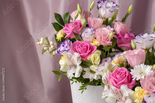floral arrangement of roses, daisies, lisianthus, chrysanthemums, unopened buds on a background of pink silk fabric with pleats.
