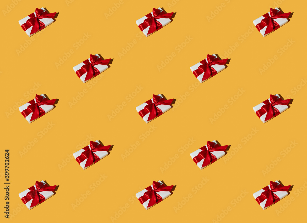 Fototapeta premium Gift pattern. Orange seamless background. Party decor. Long-distance present. Symmetrical composition of white boxes with red ribbon bows isolated on bright yellow.