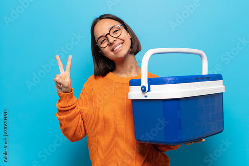 young latin woman smiling and looking friendly, showing number two or second with hand forward, counting down photo