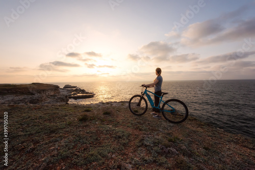 Woman with a bike in the nature / Morning view of a woman with an electric bike enjoys the view of sunrise at the rocky Black Sea coast.