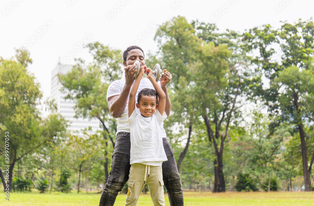 Cheerful african american father and son playing exercising with dumbbell in park, Happiness family concepts