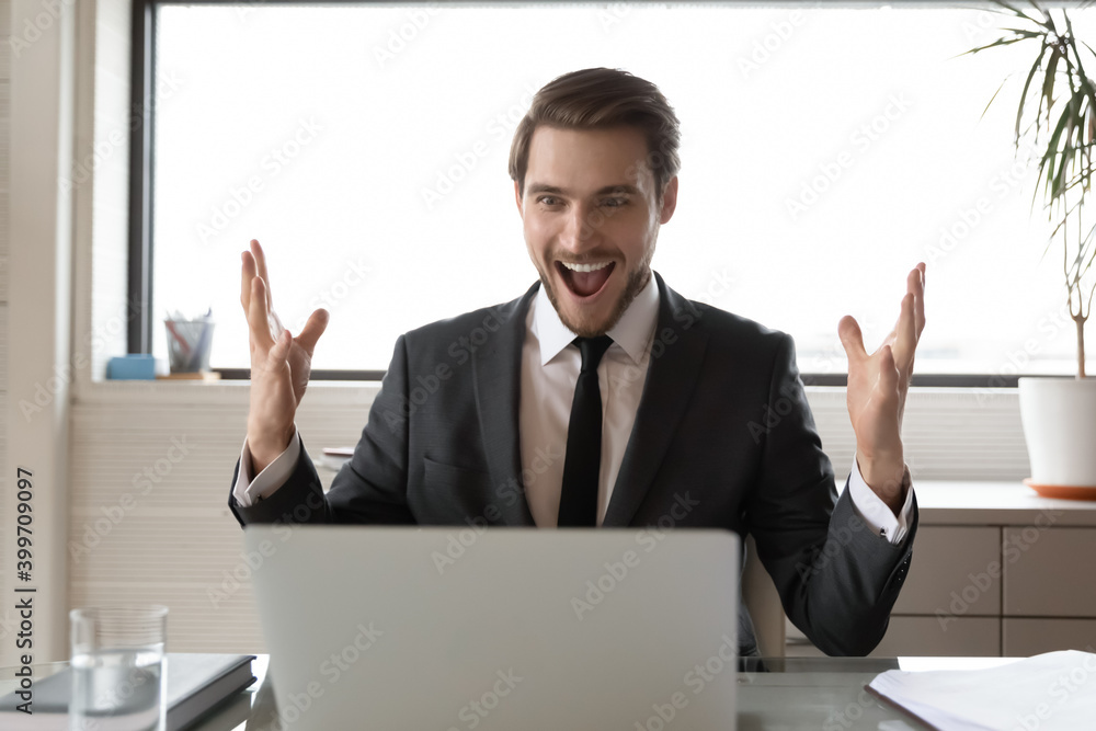 Overjoyed young Caucasian businessman feel euphoric read good amazing news online on laptop. Excited male CEO sit at desk in office triumph get business win on computer. Luck, success concept. Overjoyed young Caucasian businessman feel euphoric read good amazing news online on laptop. Excited male CEO sit at desk in office triumph get business win on computer. Luck, success concept.
