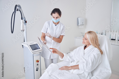 Happy smiling client looking to the list with programs of ultrasound modern machine in beauty center