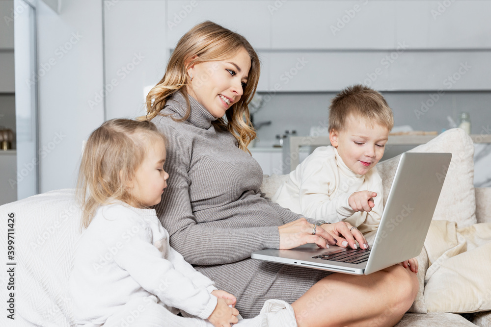 Smiling blonde mom with small children works at home in a laptop. Remote work and distance learning. Smiling blonde mom with small children works at home in a laptop. Remote work and distance learning.