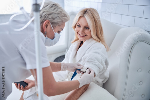 Pretty Caucasian woman in white bathrobe sitting in cosmetic armchair in beauty clinic
