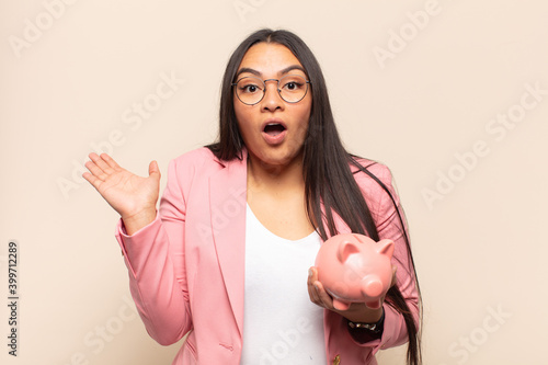 young latin woman looking surprised and shocked, with jaw dropped holding an object with an open hand on the side photo