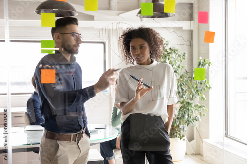 Fotografija Diverse young multiethnic employees work with sticker notes develop business startup ideas on glass wall in office