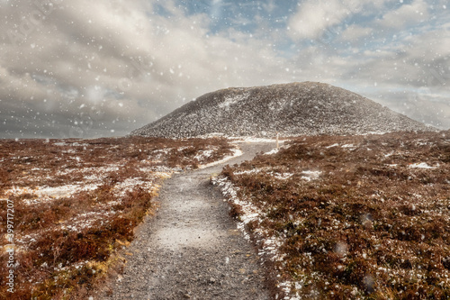 Walking path leads to Meabh's Cairn, at the summit of Knoncknarea hill, county Sligo, Ireland at winter season. Snow fall, Cloudy sky in the background. Nobody photo