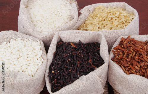 Different kinds of rice in burlap sacks - white, brown, red and black rice.