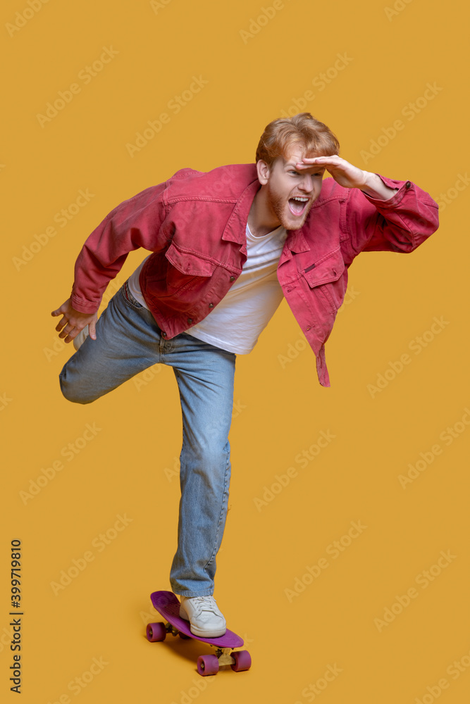 Fototapeta premium Ginger young man in red jacket with a skateboard