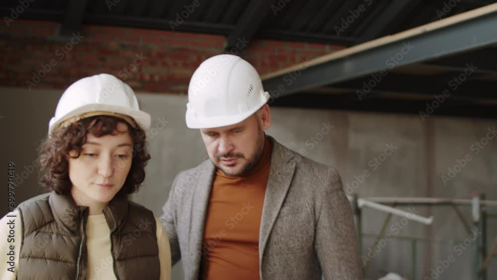 Professional male engineer in hardhat walking with female colleague at construction site and discussing job Professional male engineer in hardhat walking with female colleague at construction site and discussing job