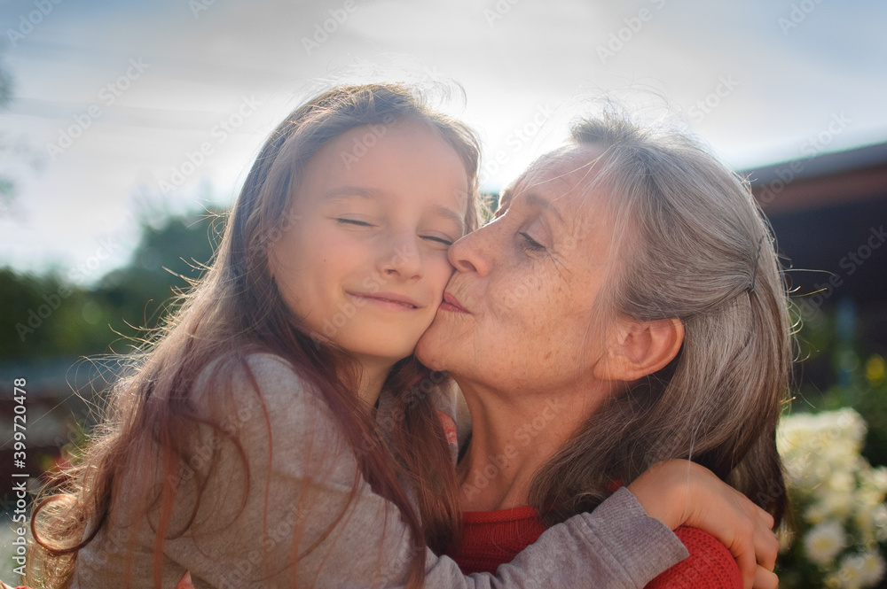 Senior grandmother with gray hair wearing red sweater with her little granddaughter are hugging in the garden and during sunny day outdoors, mother's day Senior grandmother with gray hair wearing red sweater with her little granddaughter are hugging in the garden and during sunny day outdoors, mother's day