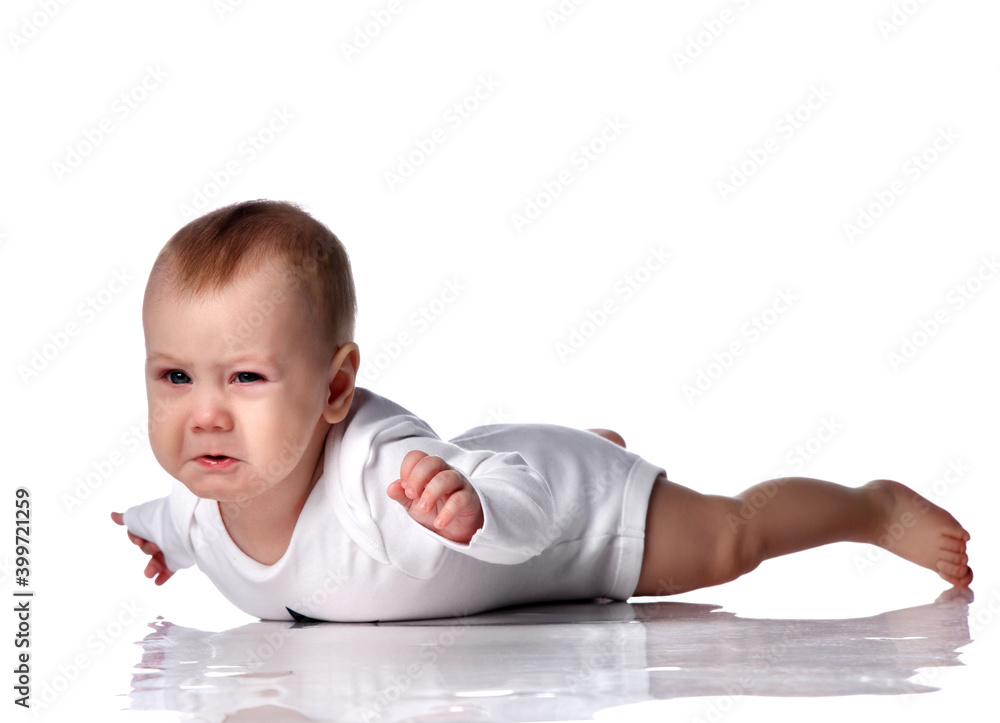 Angry disappointed infant baby boy toddler in diaper and white bodysuit with long sleeves is lying on floor on his stomach holding hands up, crying over white background. Infancy and babyhood concept Angry disappointed infant baby boy toddler in diaper and white bodysuit with long sleeves is lying on floor on his stomach holding hands up, crying over white background. Infancy and babyhood concept