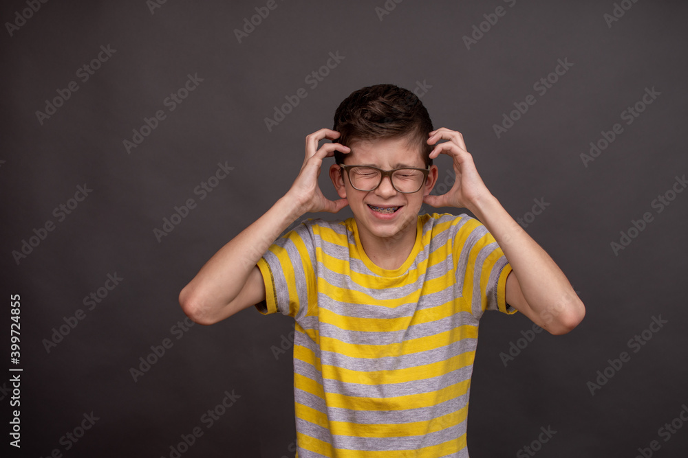 The boy is very emotional and tense, screaming in pain, holding his head. Boy is having panic attack screaming. On a gray background. Banner. A boy with glasses. High quality photo