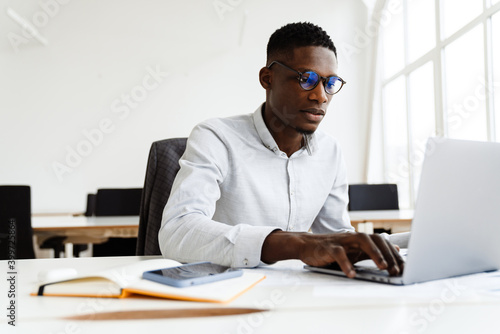 Valokuva Afro american focused man in eyeglasses working with laptop