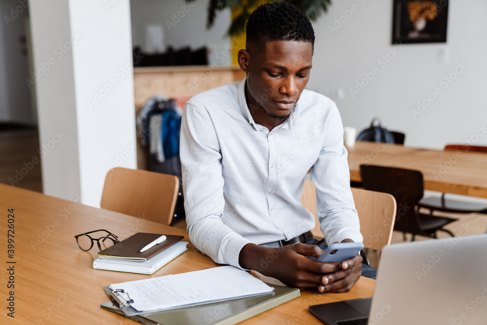 Afro american focused man using mobile phone while working with laptop Afro american focused man using mobile phone while working with laptop