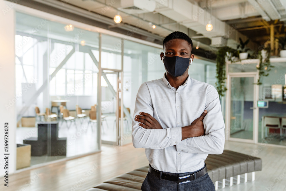 Fototapeta premium Afro american young man in face mask and earphones standing indoors