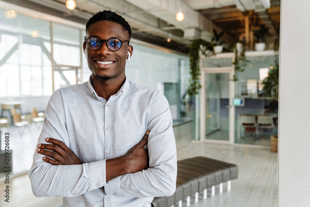 Afro american young man in eyeglasses and earphones standing indoors Afro american young man in eyeglasses and earphones standing indoors