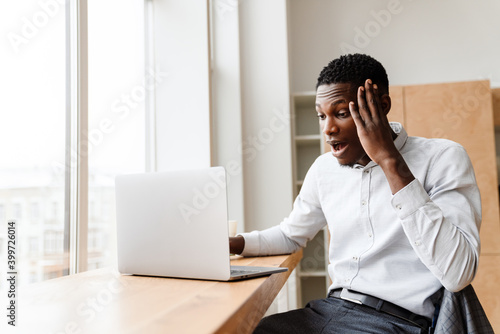 Afro american shocked man expressing surprise while working with laptop