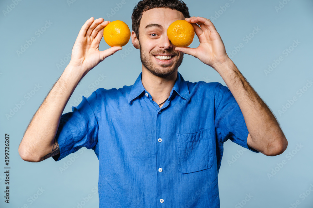 Joyful handsome guy smiling while making fun with mandarins Joyful handsome guy smiling while making fun with mandarins