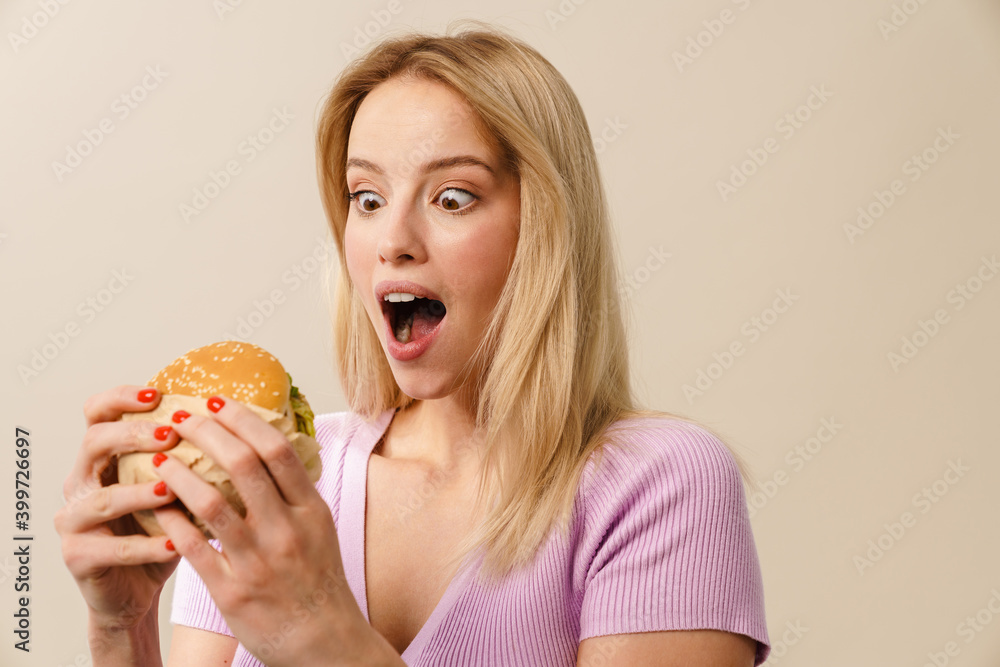 Surprised beautiful blonde girl posing with hamburger Surprised beautiful blonde girl posing with hamburger