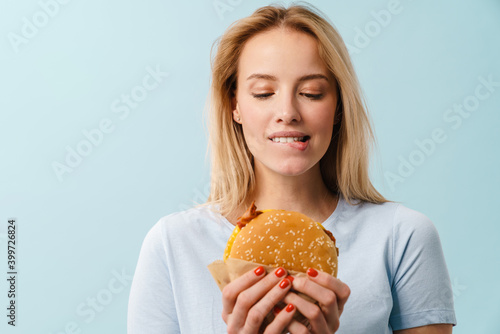 Pleased beautiful blonde girl posing with hamburger