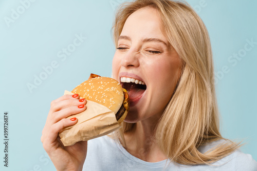 Cheerful hungry blonde girl eating hamburger on camera