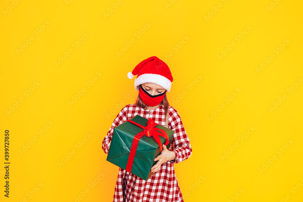 Child holding large boxes with gifts. There is a Santa hat on her head, and a medical mask on her face. Christmas mood. A perfect photo for a Christmas advertisement during a pandemic