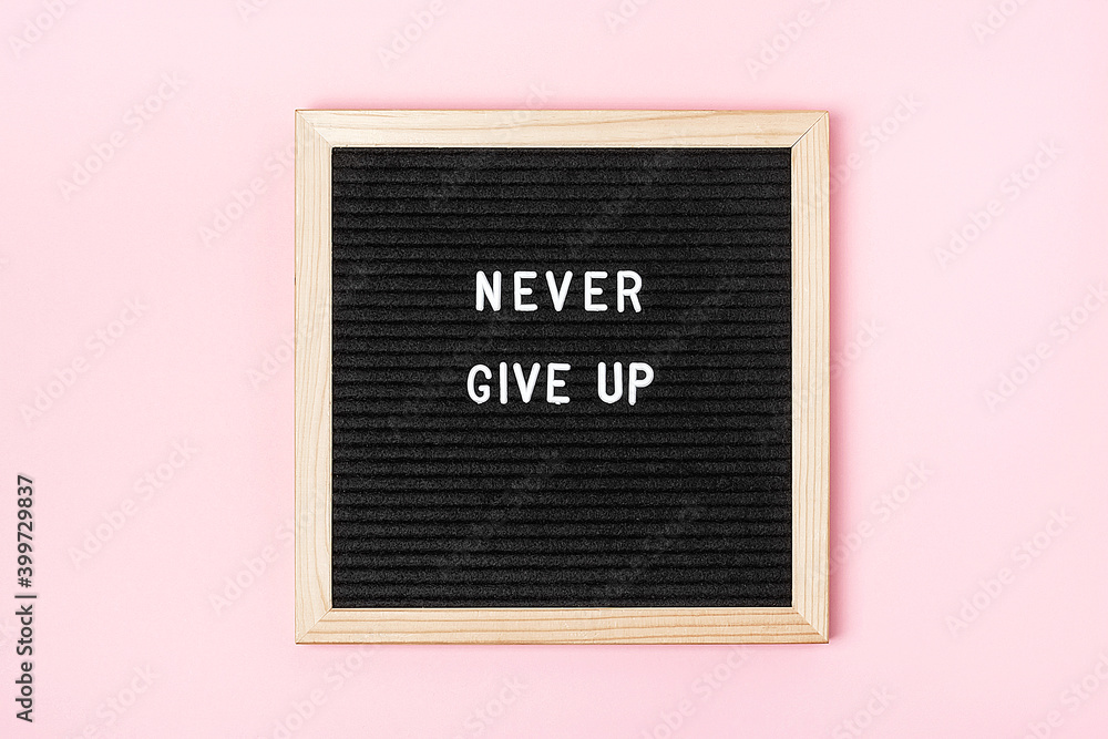 Fototapeta Never give up. Motivational quote on black letter board on pink background. Concept inspirational quote of the day. Greeting card, postcard