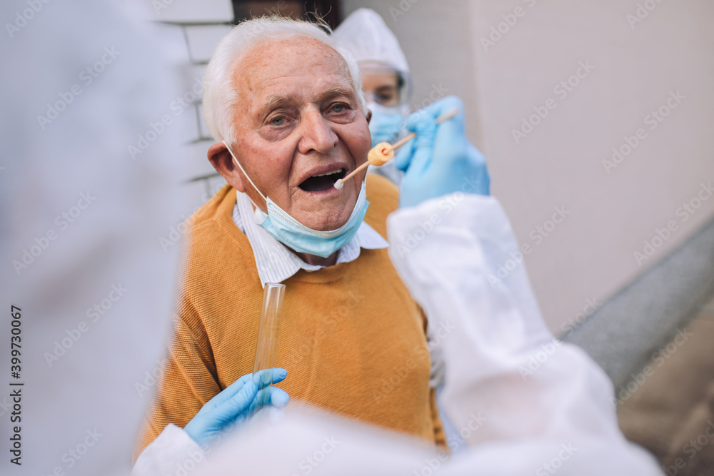 Doctors in a protective suit taking swab from a senior man to test for possible coronavirus infection. Taking corona virus test sample at home concept, senior man in quarantine. Doctors in a protective suit taking swab from a senior man to test for possible coronavirus infection. Taking corona virus test sample at home concept, senior man in quarantine.