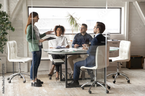 Young female team leader lead meeting with multiracial businesspeople in office. Diverse multiethnic colleagues coworkers gather in boardroom brainstorm discuss ideas in group at briefing.