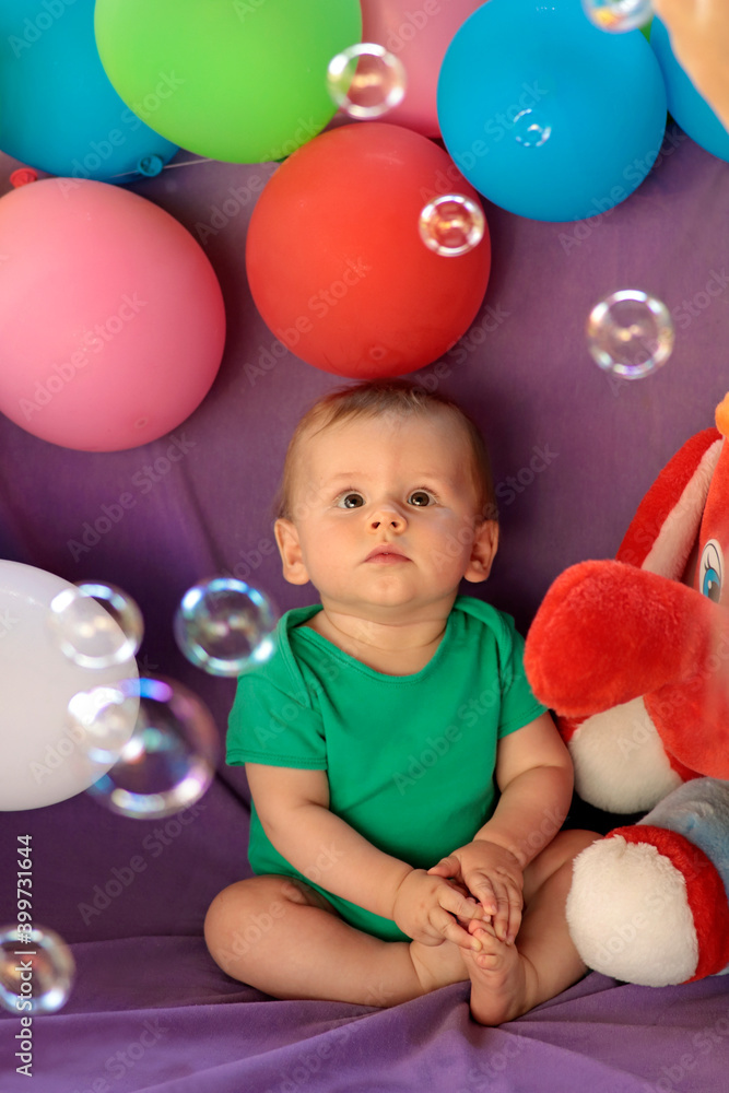 Obraz premium A little kid is sitting in a fun festive atmosphere with balloons and watching soap bubbles.