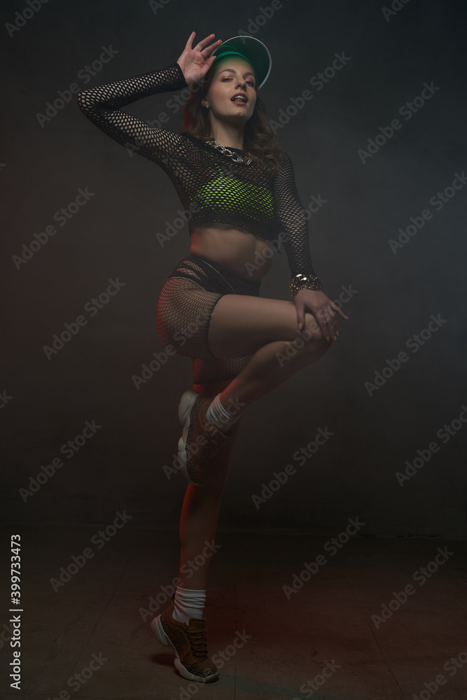 Charming graceful female model with slim figure dressed in black reticulated clothing with green cap posing in dark background. Charming graceful female model with slim figure dressed in black reticulated clothing with green cap posing in dark background.