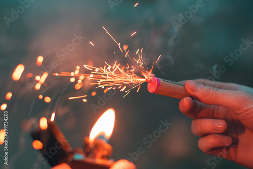 Young Man Lighting Up Firecracker in his Hand Using Gasoline Lighter. Guy Getting Ready for New Year Fun with Fireworks or Pyrotechnic Products - CloseUp Shot, Rear View