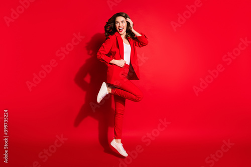Full length profile photo of pretty young lady jump look empty space wear jacket pants sneakers isolated red color background