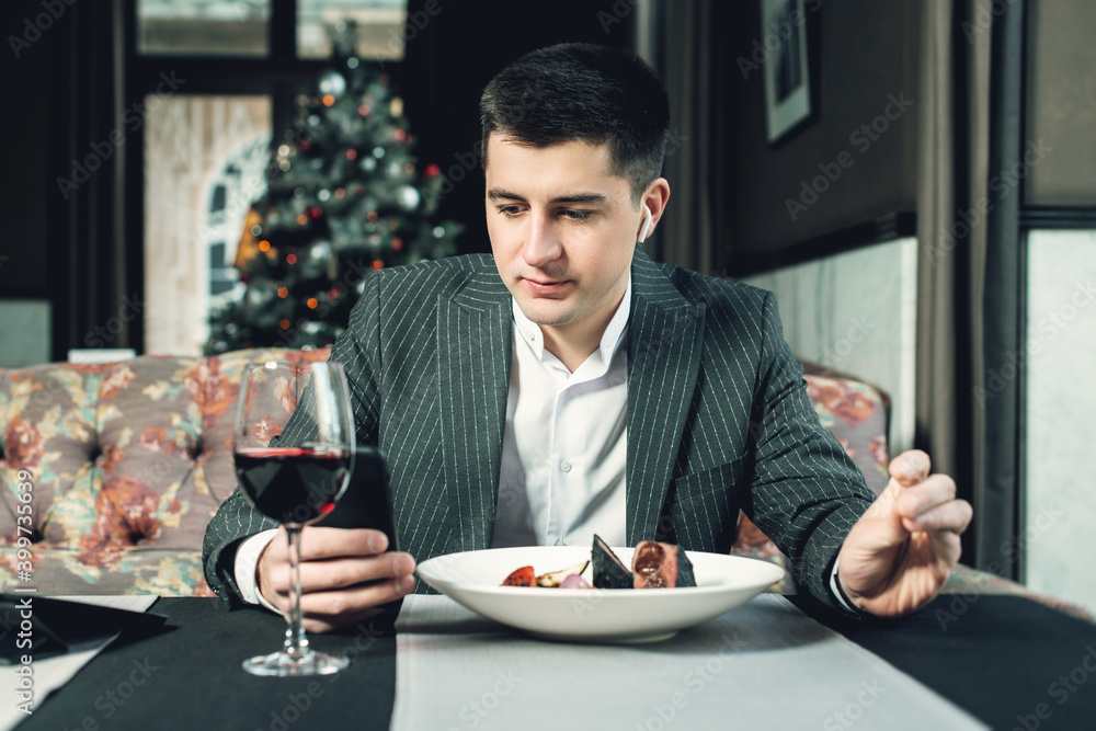 A young and attractive man uses his phone while eating veal tenderloin in ashes with grilled vegetables in an indoor restaurant A young and attractive man uses his phone while eating veal tenderloin in ashes with grilled vegetables in an indoor restaurant