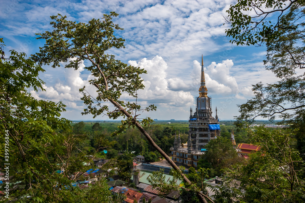 Tall Buddhist temple with spire Tiger Cave in Krabi province in Thailand through trees. Blue sky with clouds.