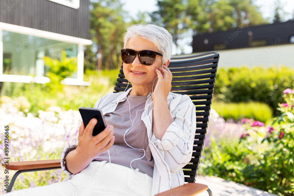 old age, retirement and people concept - happy senior woman in sunglasses with earphones and smartphone listening to music at summer garden